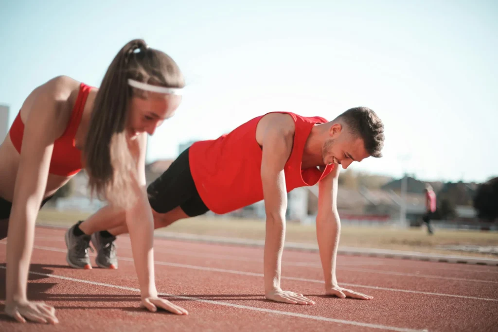 A girl and a boy performing push-ups on a grassy ground, dressed in a gym suit, demonstrating proper exercise form in an outdoor workout session.